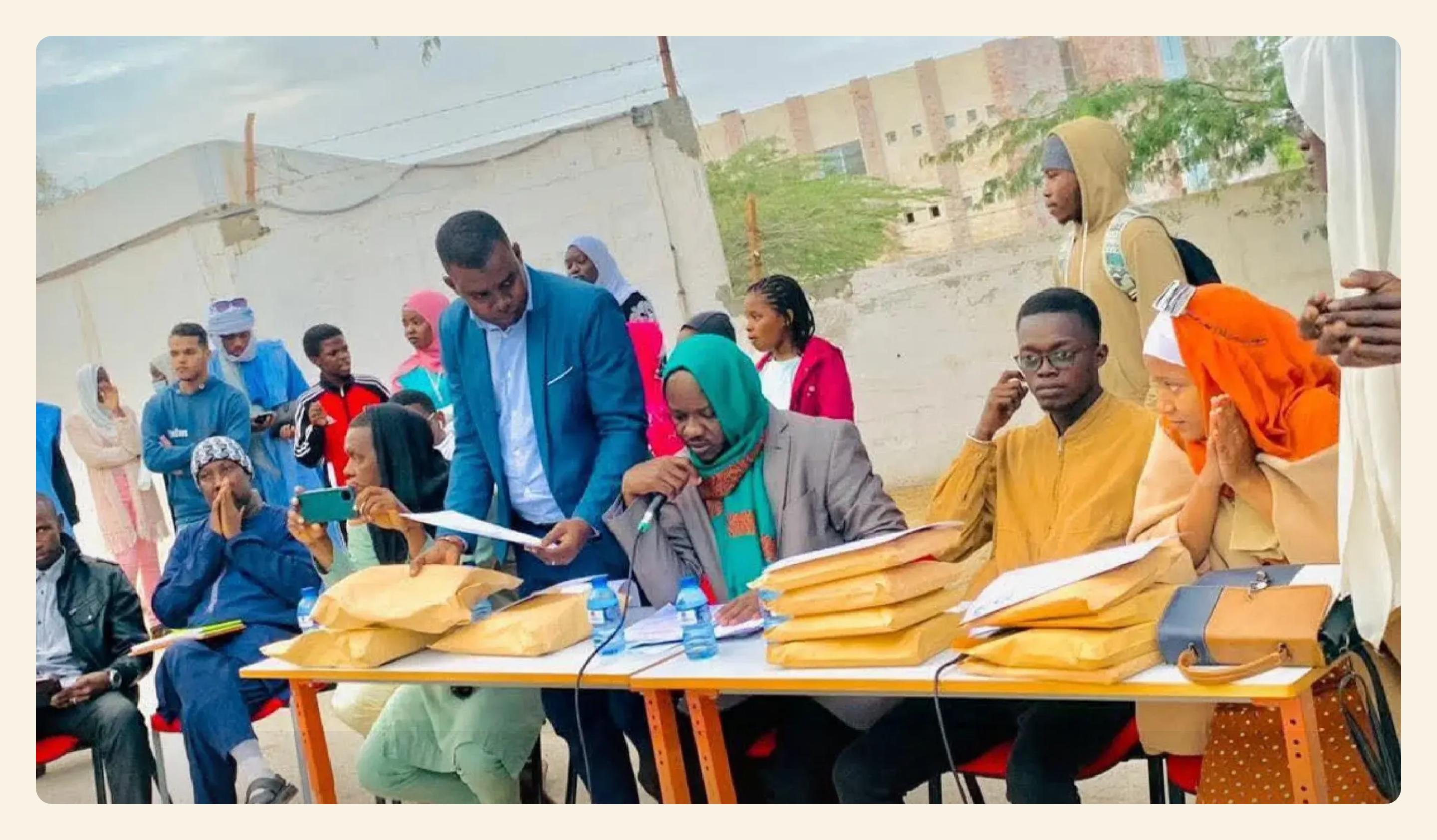 Image principale d’une page d’activité de PAYA : lors d’une cérémonie de remise de certificats, des membres du jury sont assis à une table couverte d’enveloppes, devant un public de jeunes.