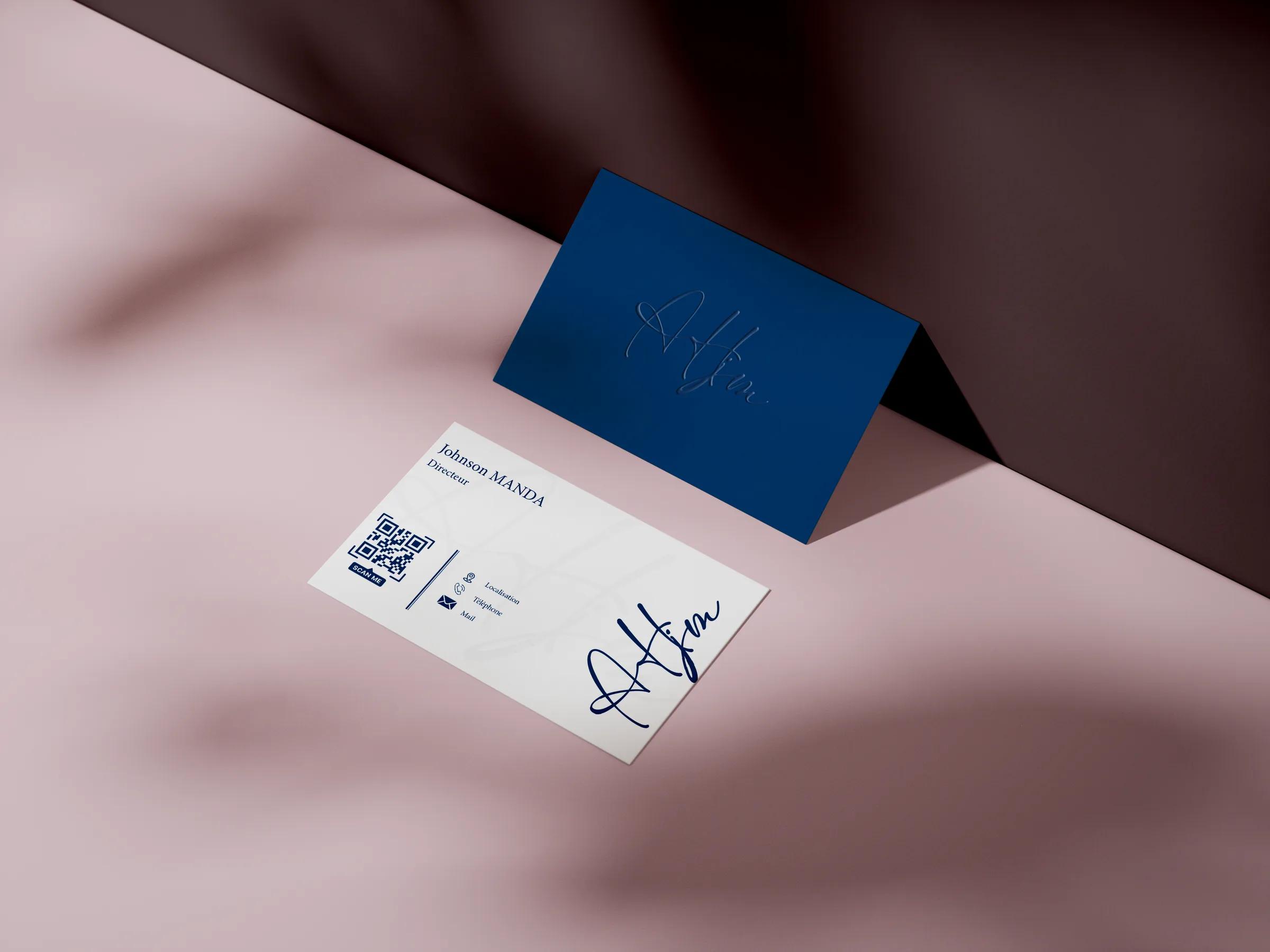 Deux cartes de visite sur un fond rose : l’une bleu marine avec une signature gaufrée, l’autre blanche avec un nom, un code QR et la même signature.