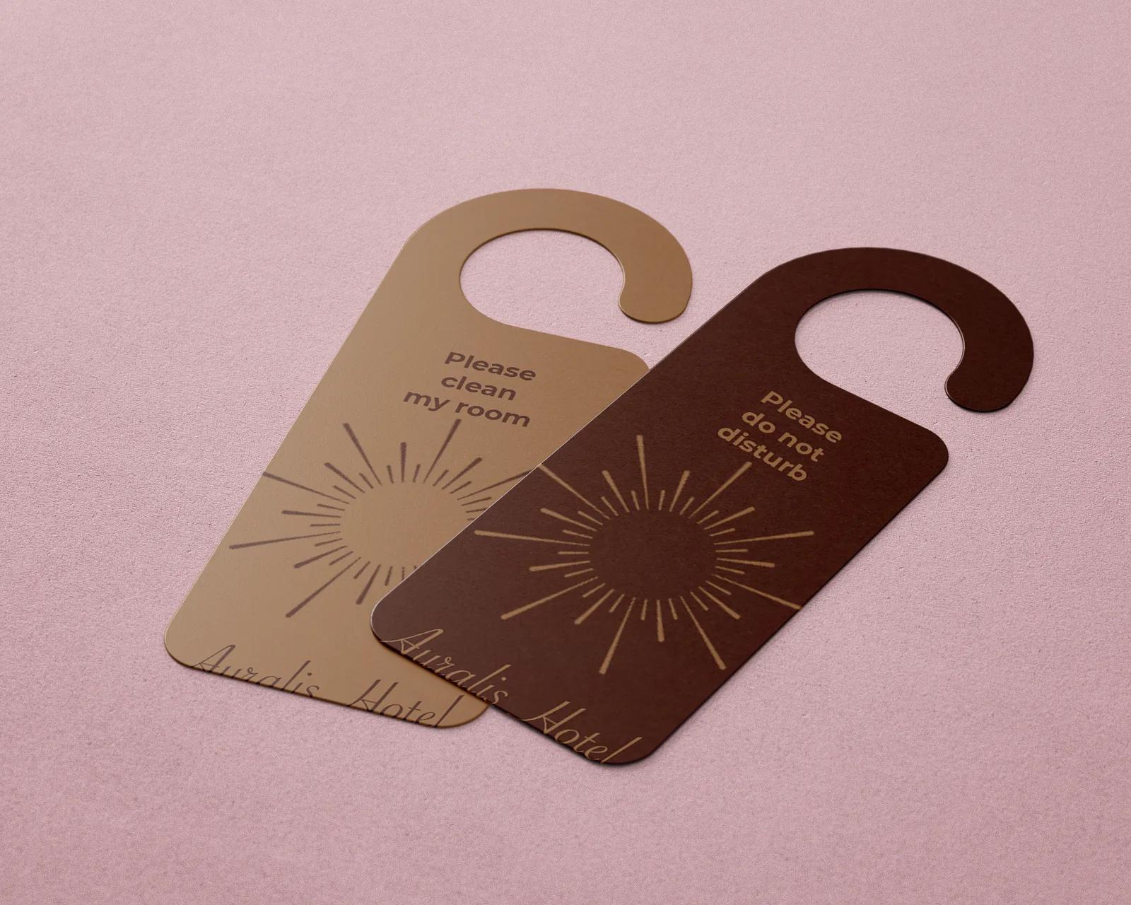 Two overlapping Auralis Hotel door hangers on a pink background, one caramel and one brown, with a sun motif, the messages “Please clean my room” and “Please do not disturb” and the script logotype.